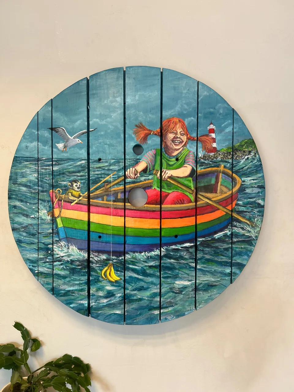 Pippi Langstrømpe ror grinende en regnbuestribet båd; i stævnen sidder en abe, en måge flyver forbi, og bag dem står et rødhvidt fyrtårn på kysten.
